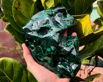 May include: A large, green malachite stone with a rough, natural texture. The stone has a deep green color with swirls and patterns throughout.