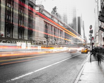 Pode incluir: Uma fotografia a preto e branco de uma rua da cidade com um táxi amarelo e um ponto de ônibus. A rua é ladeada por edifícios altos, e a foto é tirada de um ângulo baixo, olhando para os edifícios. A foto é tirada com uma longa exposição, por isso os carros e as pessoas na rua estão desfocados.