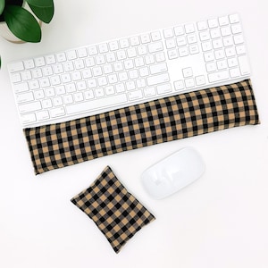 May include: A rectangular keyboard wrist rest and a smaller square mouse wrist rest, both featuring a black and tan buffalo check pattern. These fabric-covered cushions are positioned below a white wireless computer keyboard and a white computer mouse.