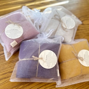 May include: Four heat therapy packs in different colors, wrapped in white mesh bags with twine and a label that says "Instructions: Heat Therapy".