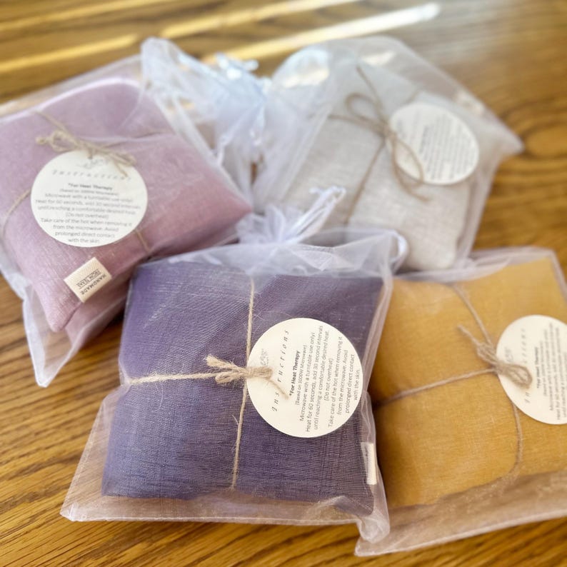 May include: Four heat therapy packs in different colors, wrapped in white mesh bags with twine and a label that says "Instructions: Heat Therapy".