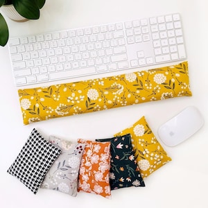 May include: A white keyboard and mouse are next to a yellow floral print wrist rest. Below are five small, square pillows in various patterns: black and white houndstooth, gray floral, orange floral, dark green floral, and yellow floral.