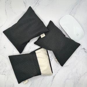 May include: Three black and white patterned eye pillows with a white label that says "Hello Harmony". The pillows are on a white marble surface with a white computer mouse.