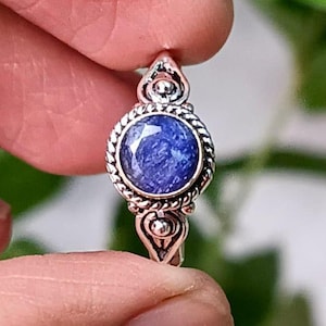Può includere: Un anello d'argento con una pietra preziosa blu incastonata in una montatura decorativa. L'anello presenta un design dettagliato con piccole perle e motivi intricati.