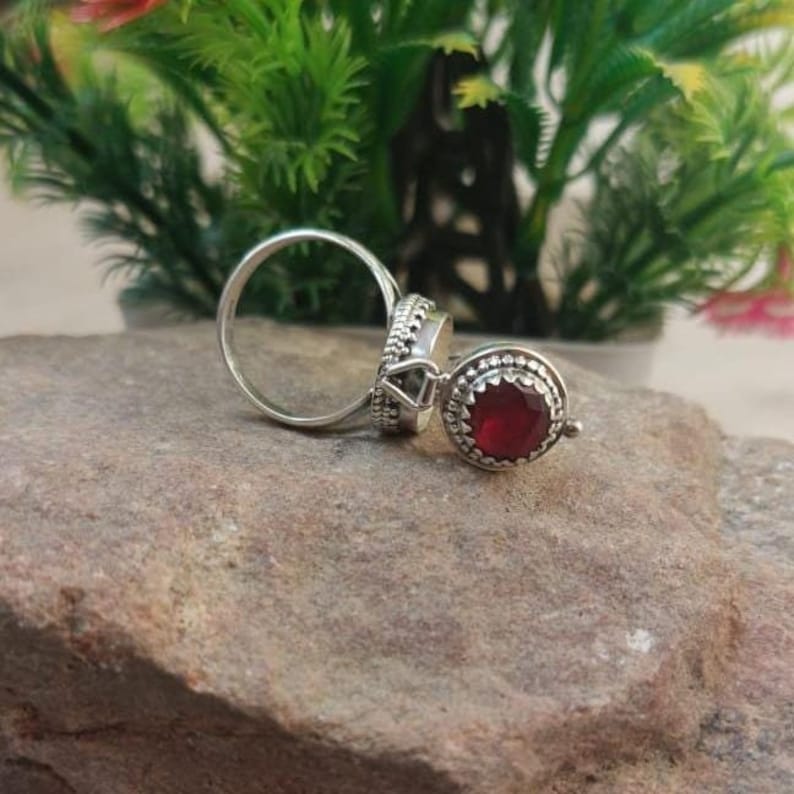 K&ouml;nnte beinhalten: Ein silberner Ring mit einem roten Edelstein, der in einer runden Fassung sitzt. Der Ring ist mit filigranen Details verziert und hat ein zartes Design.
