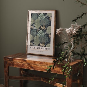 Peut inclure: Une affiche encadr&eacute;e avec un design vintage repr&eacute;sentant un motif r&eacute;p&eacute;titif d'arbres, de cerfs et d'oiseaux sur un fond bleu fonc&eacute;. L'affiche est intitul&eacute;e "William Morris" et comprend le texte "The Victoria & Albert Museum, London".
