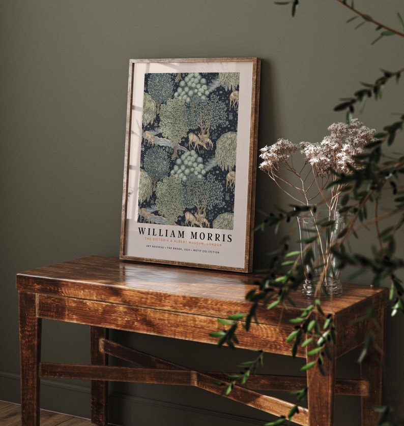 Peut inclure: Une affiche encadr&eacute;e avec un design vintage repr&eacute;sentant un motif r&eacute;p&eacute;titif d'arbres, de cerfs et d'oiseaux sur un fond bleu fonc&eacute;. L'affiche est intitul&eacute;e "William Morris" et comprend le texte "The Victoria & Albert Museum, London".