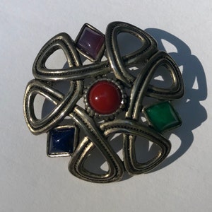 May include: A silver-toned Celtic knot brooch with four colored stones. The stones are red, green, blue, and purple.