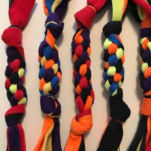 May include: Five colorful braided dog toys made from fabric scraps. Each toy features a combination of bright colors like red, orange, blue, yellow, and purple. The toys are knotted at both ends and have a braided central section.