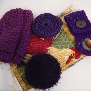 May include: Purple knitted dishcloths and scrubbers. The scrubbers are round and have a textured surface. The dishcloths are rectangular and have a smooth surface. The dishcloths and scrubbers are arranged on a fabric background with a rooster design.
