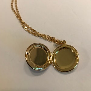 May include: A gold locket necklace with a round, hinged locket. The locket is open, revealing two empty compartments.