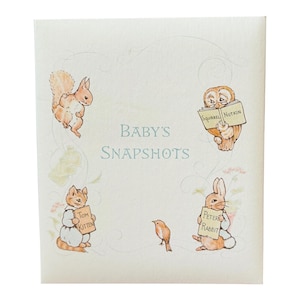 May include: A square off-white photo album cover with the text Baby's Snapshots in blue. The cover features illustrations of a squirrel, an owl reading a book titled Squirrel Nutkin, a kitten holding a sign saying Tom Kitten, and Peter Rabbit.