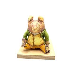 May include: A plush toy mouse wearing a green jacket and yellow pants, sitting on a wooden base.