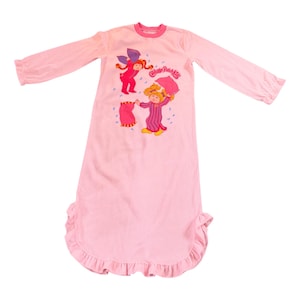 May include: A light pink Cabbage Patch Kids nightgown with long sleeves and a ruffled hem. The front features a graphic of two Cabbage Patch Kids characters, one holding an umbrella. The nightgown has a round neckline and is made of a soft fabric.