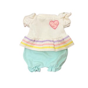 May include: A one-piece outfit featuring a white bodice with short ruffled sleeves and a pink heart applique. The waist has a ruffled trim with horizontal pastel stripes in purple, pink, and yellow, transitioning into light mint green shorts.