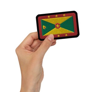 May include: Embroidered patch featuring the flag of Grenada. The rectangular patch has a black border with a red inner border. The flag design includes yellow, green, and red colors, with a central star and nutmeg image.