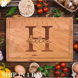May include: A rectangular wooden chopping board with a juice groove, engraved with the letter "H" and the name "Helen". The board is made of light-coloured wood and is surrounded by fresh produce, including tomatoes and eggs. The text "Made in Canada" is in the top left corner.