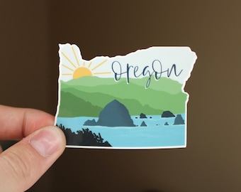 May include: A sticker featuring a stylized outline of the state of Oregon with a sunrise, mountains, and a rocky coastline. The word "Oregon" is written in cursive across the top of the sticker.