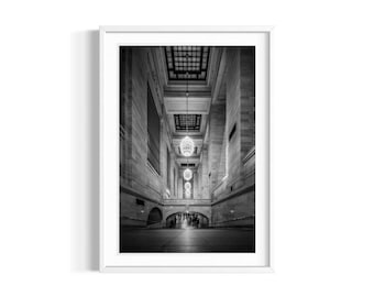 May include: A black and white photograph of a grand hall with a high ceiling and a row of ornate chandeliers. The hall is empty except for a few people walking in the distance.