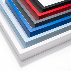 May include: An angled view of a stack of picture frames in various colors. The frames are white, light blue, blue, dark gray, red, and black. The frames are made of wood and have a clean, modern design.