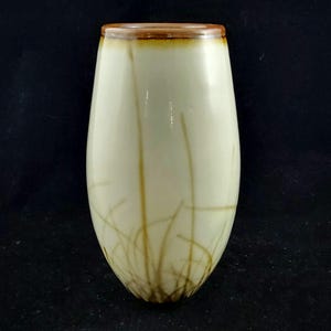 Könnte beinhalten: Eine weiße Keramikvase mit braunem Rand und einem Design aus braunen Linien, die an Gras erinnern.