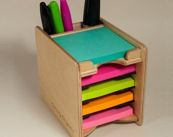 May include: Wooden desk organizer with five compartments for sticky notes. The compartments are filled with different colored sticky notes. There are four markers in the top compartment, including black, green, pink, and blue.
