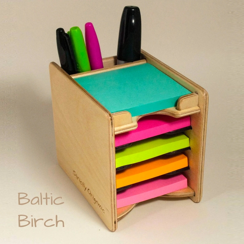 May include: A wooden desk organizer with five colorful sticky note pads. The organizer is made of Baltic birch wood and has a slot for pens and markers. The sticky notes are in shades of pink, orange, yellow, green, and blue.