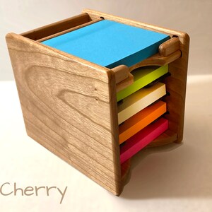 May include: A wooden note pad holder with a cherry finish. The holder has five slots for different colored note pads. The note pads are green, yellow, white, orange, and pink.