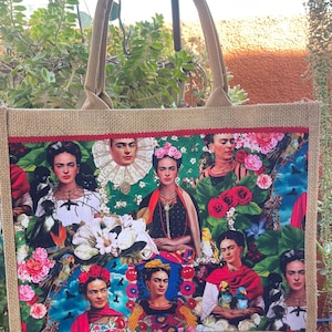May include: A rectangular tote bag with a burlap body and handles. The front features a colorful collage of Frida Kahlo portraits, flowers, and birds. The top edge is trimmed with red fabric. The bag is designed for carrying items.