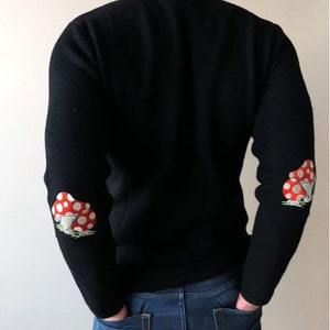 May include: Black long-sleeved sweater with red and white mushroom embroidery on the elbows.