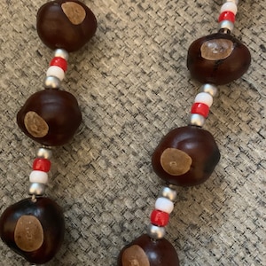 May include: A necklace made with brown buckeye nuts and silver, red, and white beads.
