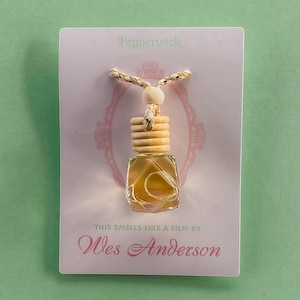 May include: A white card with pink lettering reads "Pepperwick" and "This smells like a film by Wes Anderson". A small glass bottle with a wooden stopper hangs from a gold cord.