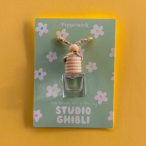 May include: A green card with white flowers and the text "Pepperwick" and "this smells like a film by STUDIO GHIBLI" with a small glass bottle hanging from a string with wooden beads.