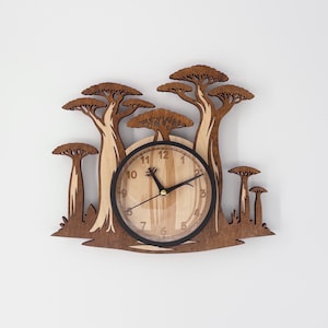 May include: Wooden wall clock featuring a nature-inspired design. The clock face is surrounded by a laser-cut depiction of trees in shades of brown. The clock hands are black, and the numbers are visible on the clock face.