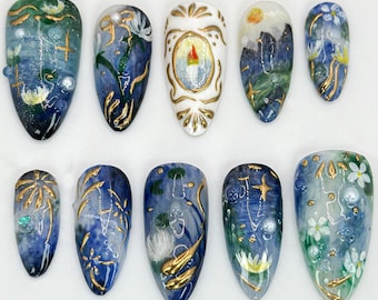 May include: Set of ten blue and white nail art tips with gold accents. Each tip features a different design, including flowers, stars, and geometric patterns.