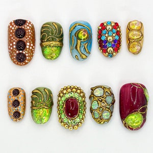 May include: Ten different nail designs featuring various colors, patterns, and embellishments. Some designs include gold accents, rhinestones, and swirls.
