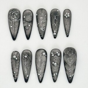 May include: Set of ten black and silver nail tips with various designs, including roses, butterflies, hearts, and vines.
