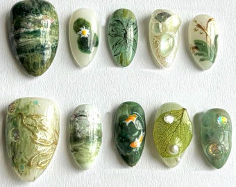 May include: Set of 10 green and white nail art designs. The designs include a water lily, a dragonfly, a leaf, a fish, and a floral pattern.