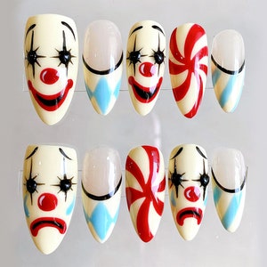 Peut inclure: Ensemble de dix faux ongles avec une vari&eacute;t&eacute; de motifs. Cinq ongles pr&eacute;sentent un visage de clown avec un nez rouge, des yeux noirs et un sourire noir. Deux ongles pr&eacute;sentent un motif de canne en sucre rouge et blanc. Trois ongles pr&eacute;sentent un motif &agrave; carreaux bleu et blanc avec un contour noir.