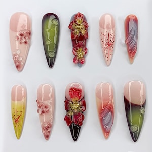 May include: Ten long, almond-shaped artificial nails with various designs. Some nails have a gradient of pink and white, others have a green and black gradient, and some have red and gold flowers.