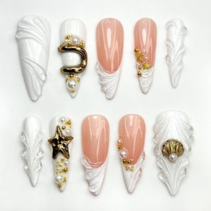 Op de afbeelding: Set van tien kunstnagels met een witte en roze basis. De nagels zijn versierd met gouden accenten, parels en schelpen.