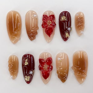 May include: Set of ten false nails with a brown swirl design, red flower accents, and gold glitter.