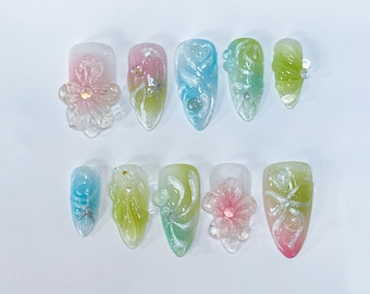 Puede incluir: Diez puntas de uñas ovaladas translúcidas y coloridas con diseños florales y en espiral. Las puntas están pintadas en tonos de rosa, azul, verde y blanco.