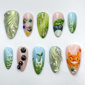 Puede incluir: Conjunto de diez uñas postizas con varios diseños inspirados en la película "Mi vecino Totoro". Los diseños incluyen un Totoro verde y blanco, un conejito blanco, espíritus de hollín negros y patrones florales verdes y blancos.