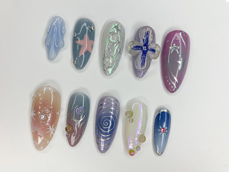 May include: Ten different nail designs featuring a variety of colors, patterns, and embellishments. The designs include stars, swirls, butterflies, and glitter.