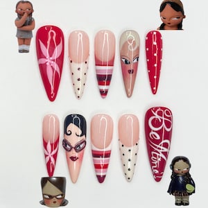May include: Ten long, almond-shaped artificial nails with diverse designs. The designs include floral patterns, polka dots, stripes, and faces. One nail features the text "Be Mine" in white script. Small figurines are placed around the nails.