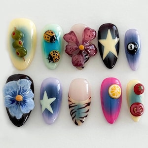 May include: Ten different nail designs featuring various themes, including ladybugs, flowers, olives, a star, a pool ball, a lemon, a zebra print, and tomatoes.