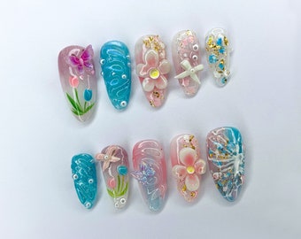 Puede incluir: Conjunto de diez uñas postizas con una variedad de diseños florales y de mariposas. Las uñas están pintadas en tonos de azul, rosa y blanco con detalles dorados.