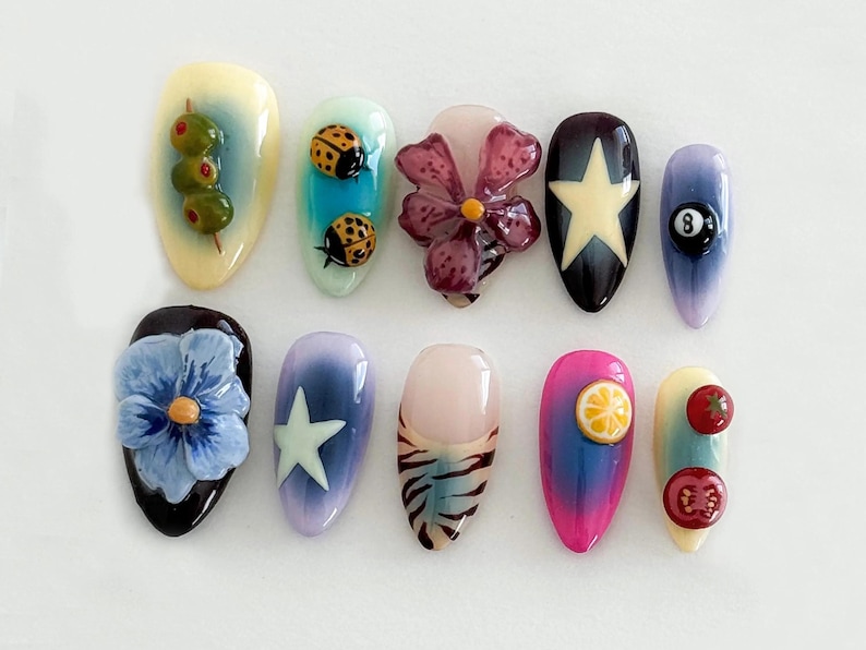 May include: Ten different nail designs featuring various 3D embellishments, including ladybugs, olives, flowers, stars, a pool ball, a lemon slice, and tomatoes.