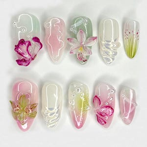 May include: Ten artificial nails with a clear base and painted floral designs. The designs include pink, white, and green flowers.